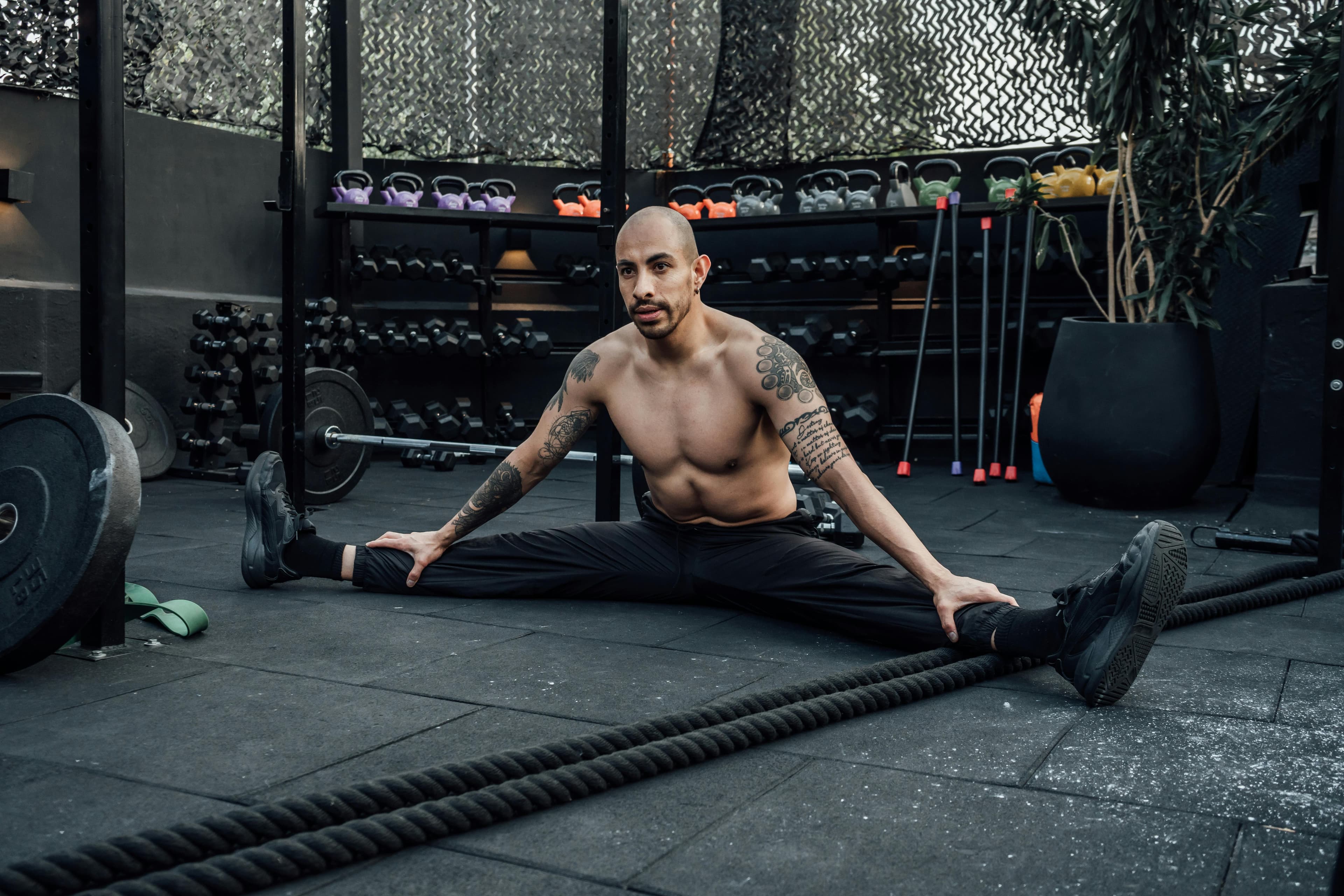 Tattooed man performing a split stretch in a gym, showcasing flexibility and fitness lifestyle in Mexico City.