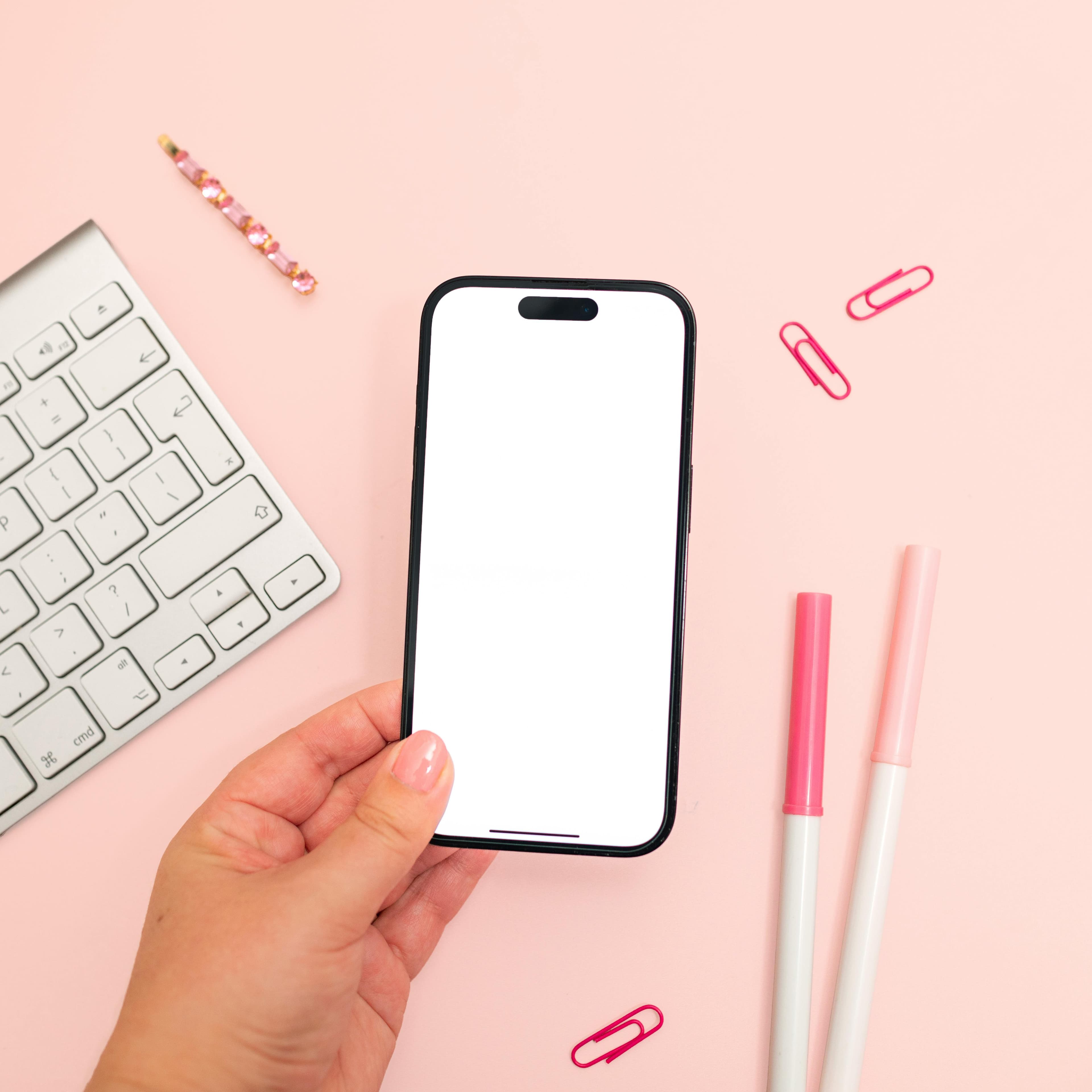 手に持ったスマートフォンのモックアップを展示した、ピンクをテーマにしたミニマルなワークスペース。