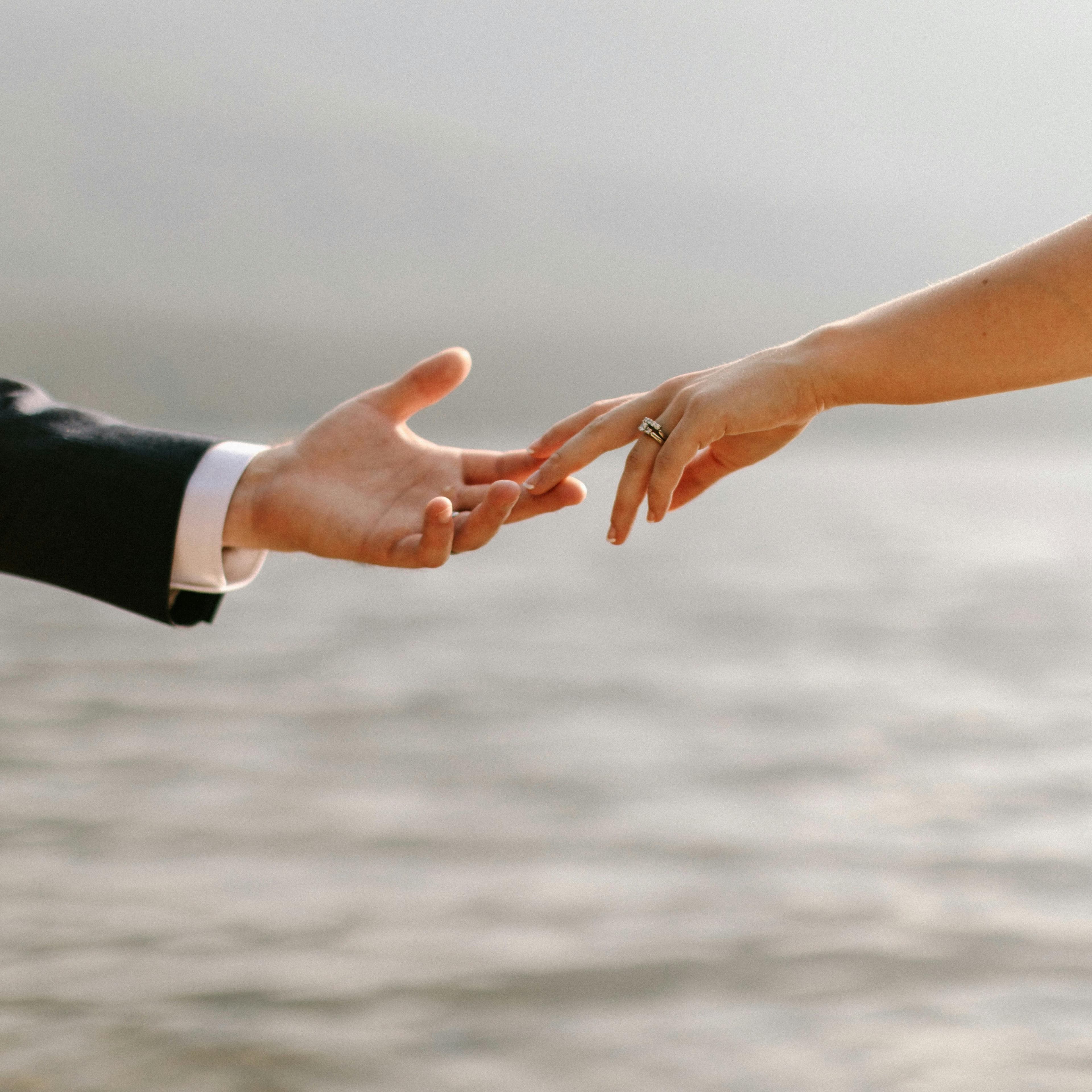 Close-up of a couple's hands showcasing wedding rings by the waterfront.
