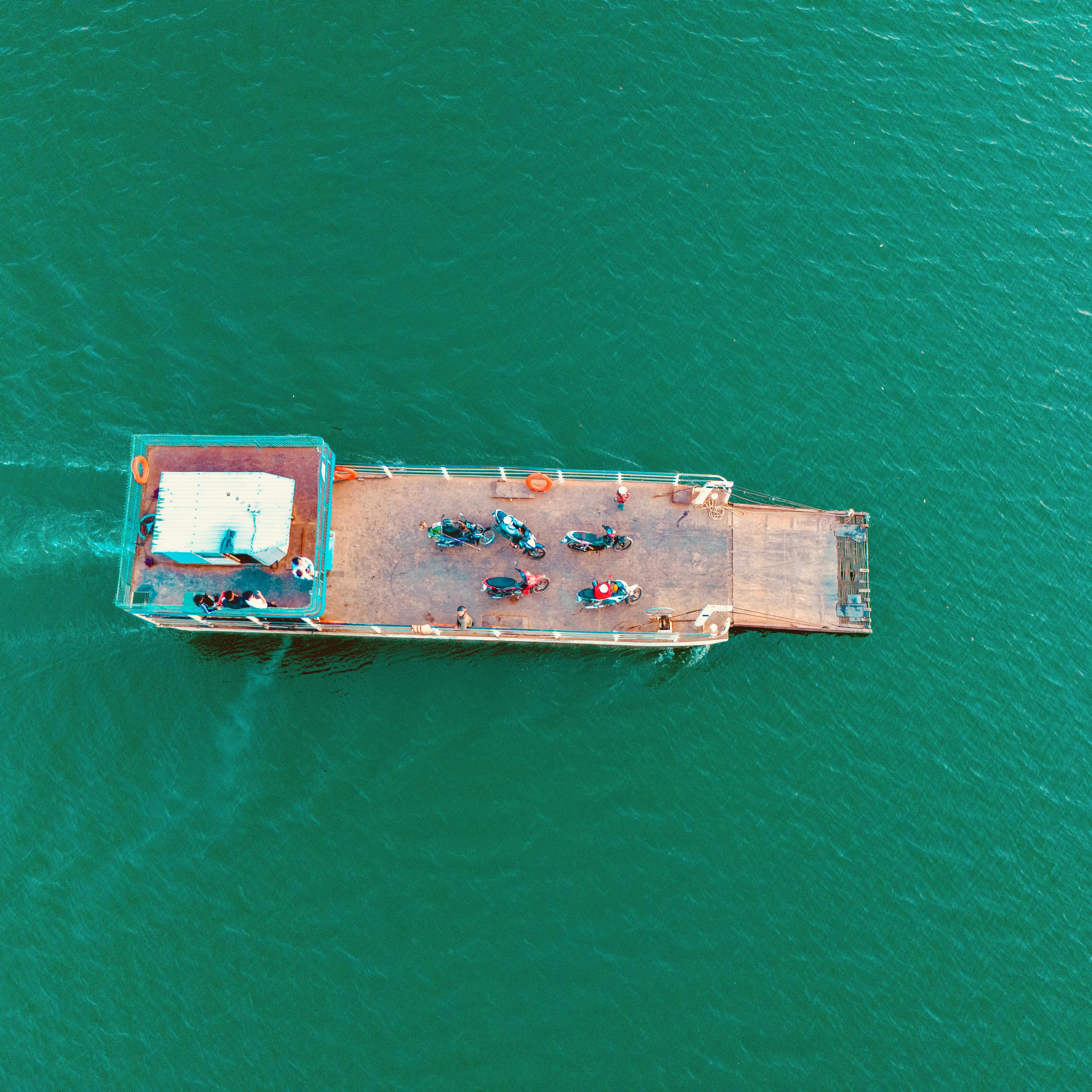 鮮やかな緑色の水面を渡ってバイクを輸送する船の空中写真。