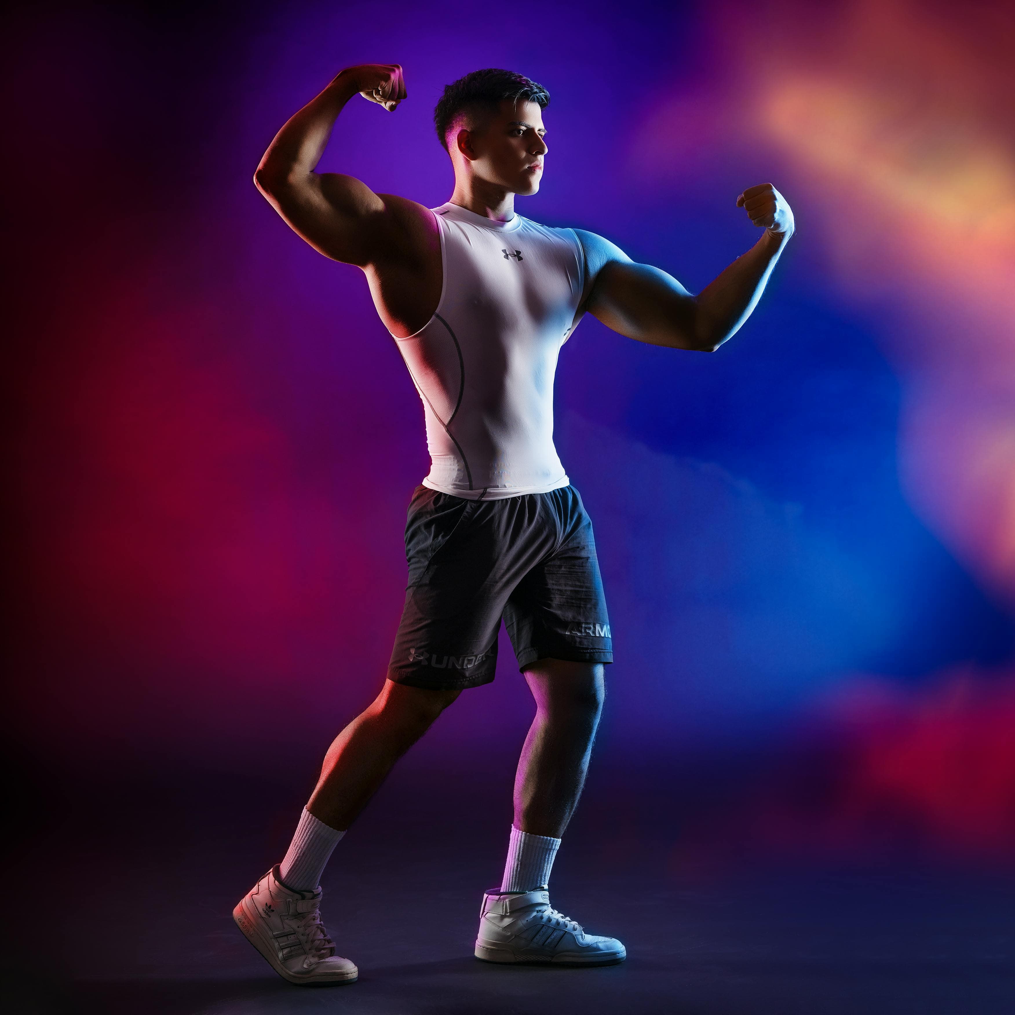 Atleta musculoso flexionando los brazos contra un fondo colorido, mostrando fuerza y aptitud física.