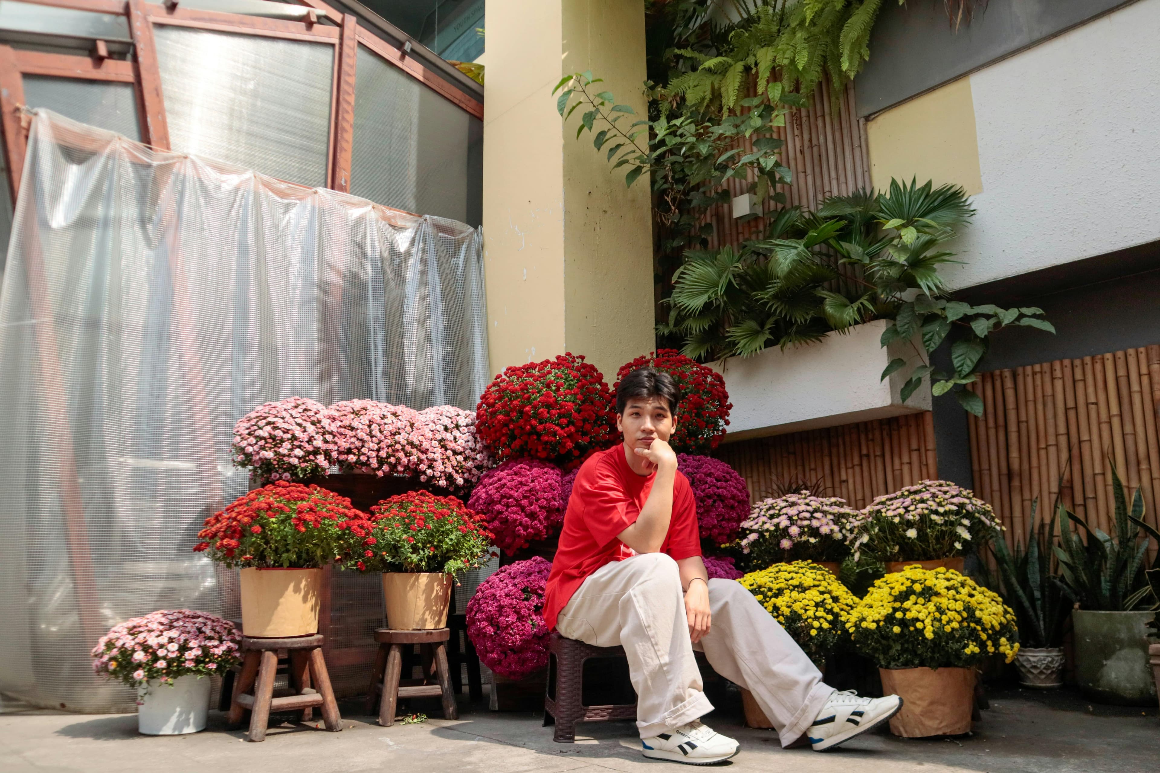 屋外の花の舞台で、鮮やかな菊に囲まれた人が座っています。