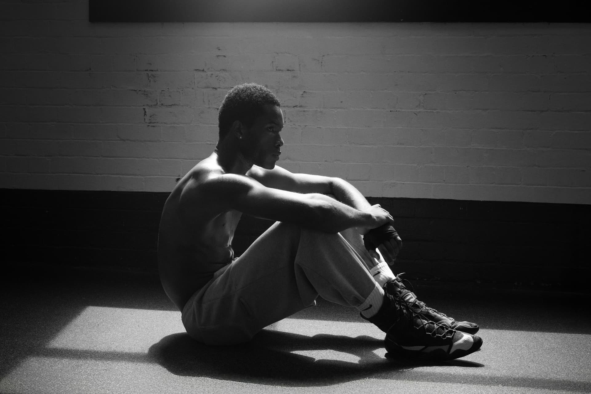 Black and white portrait of a pensive athlete sitting indoors, lit dramatically.