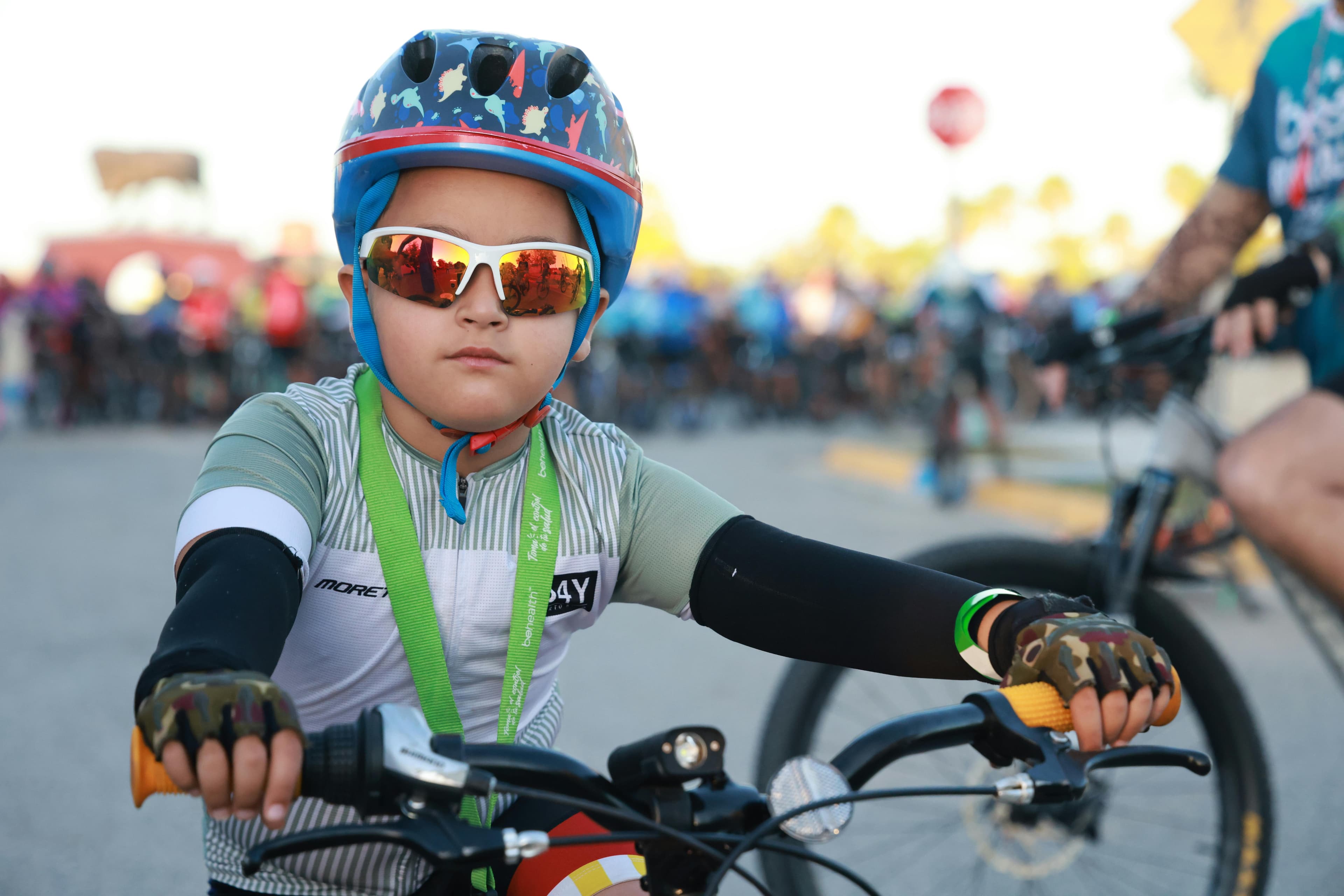 Un enfant avec un casque coloré et des lunettes de soleil participe à une compétition cycliste.