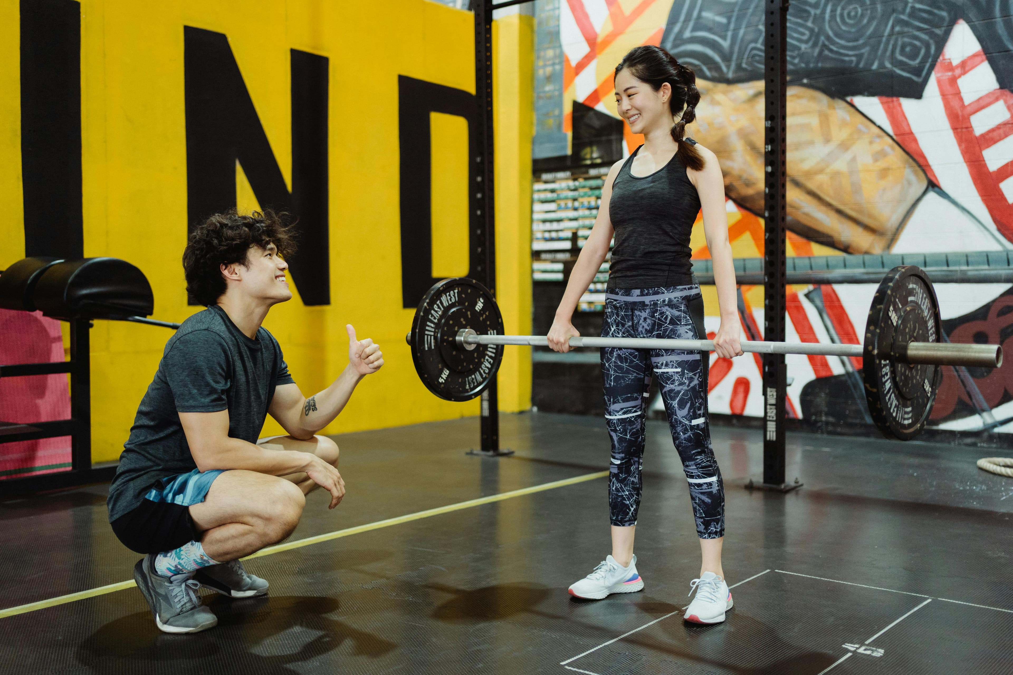 Young woman lifting weights with trainer guidance indoors, showcasing fitness and motivation.