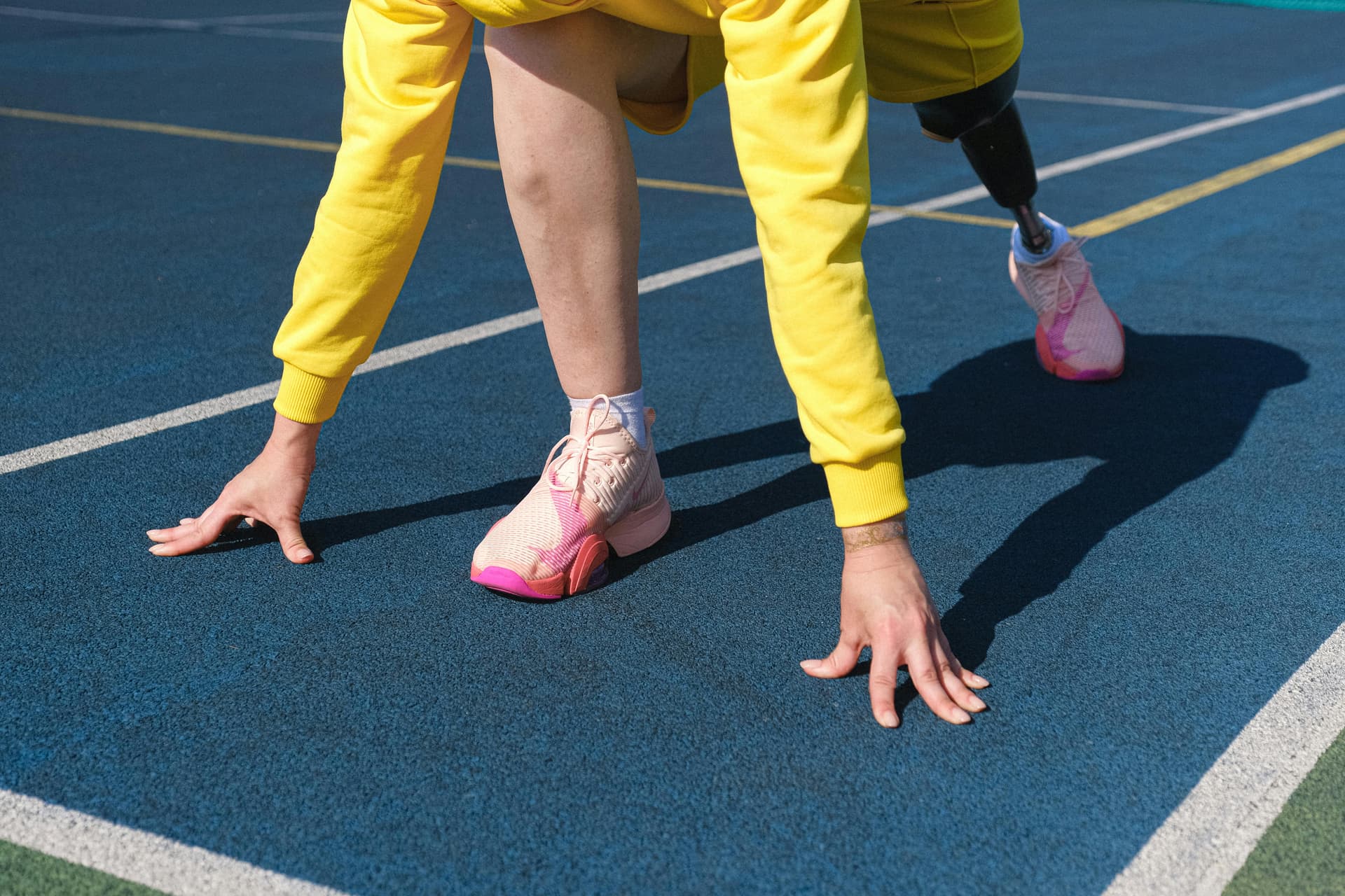 Female athlete with a prosthetic leg preparing to run on an outdoor track.