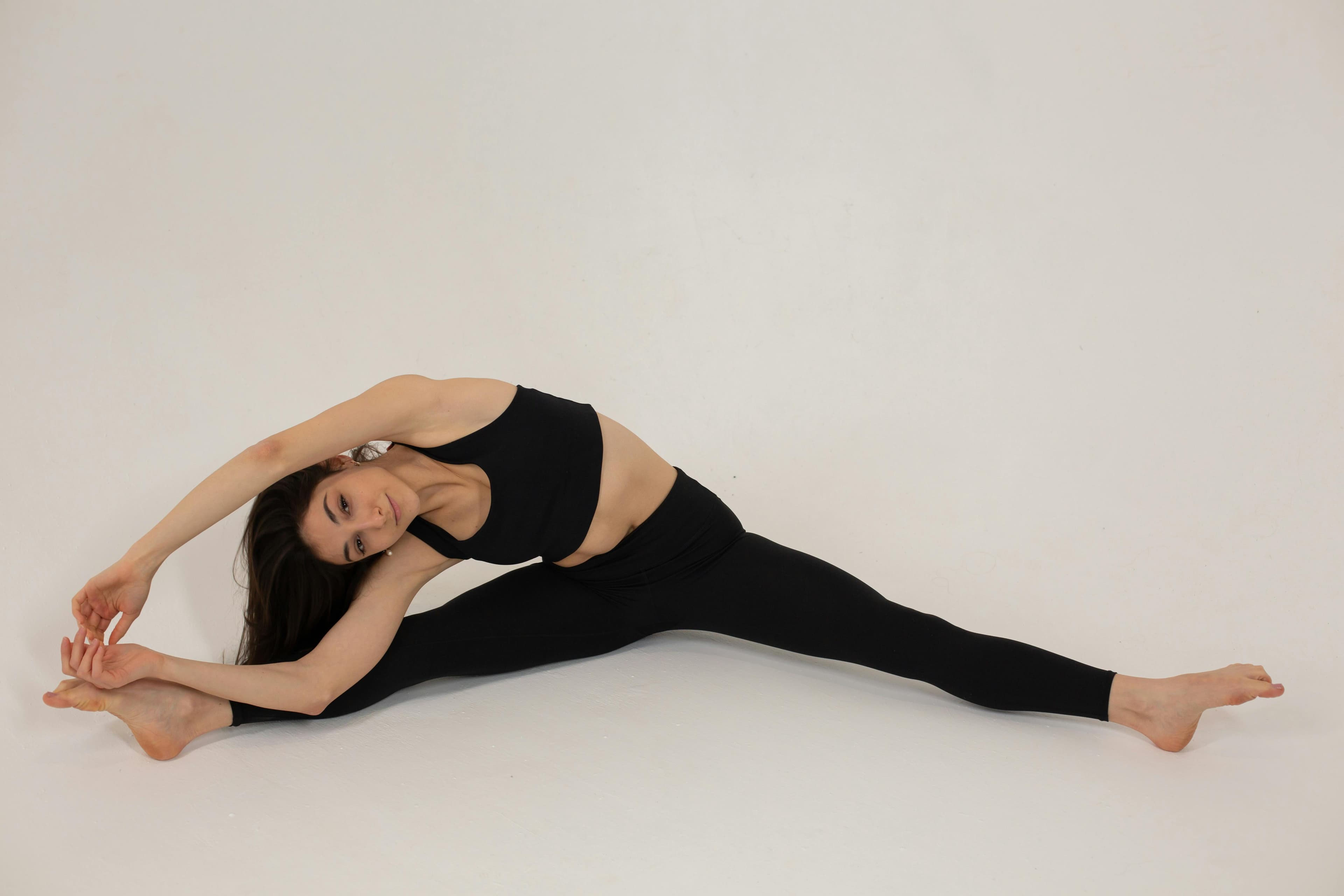 Flexible young woman performs a full split in activewear, showcasing grace and fitness on a white background.
