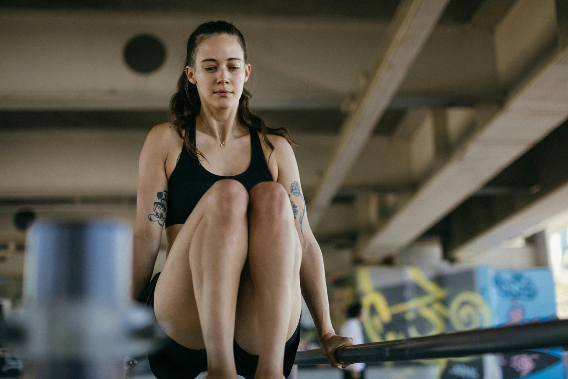 Young woman in activewear performs fitness routine on outdoor bar, showcasing strength and concentration.